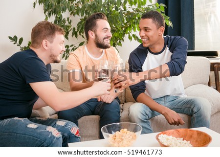 Picture of happy friends drinking alcohol drinks at home all together. Handsome men drinking beers and eating pop corn.
