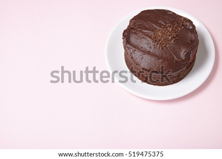 A whole chocolate fudge layer cake on a pastel pink background with blank space at side