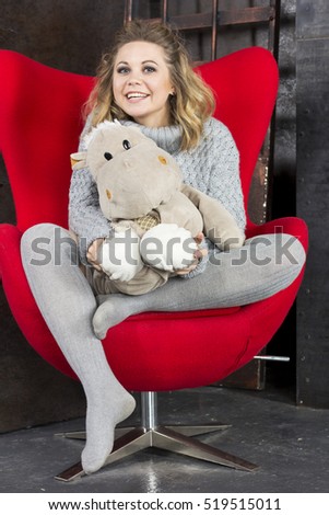 Smiling young girl sitting with soft toys on a red chair