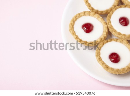 A plate full of freshly baked Bakewell tarts on a pastel pink background with blank space at side