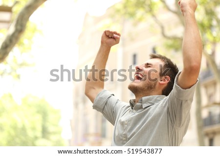 Portrait of an excited man raising arms in the street with buildings in the background Royalty-Free Stock Photo #519543877