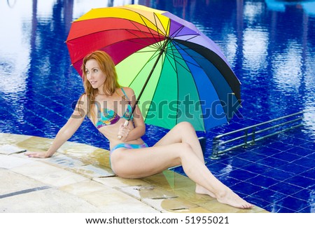 The young attractive woman at pool under a colour umbrella