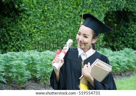 Young woman in graduation gowns holding diploma and book