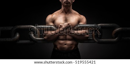 Broken Chain - Freedom Concept . Brutal man bodybuilder athlete holding a chain on a black background. metaphor
