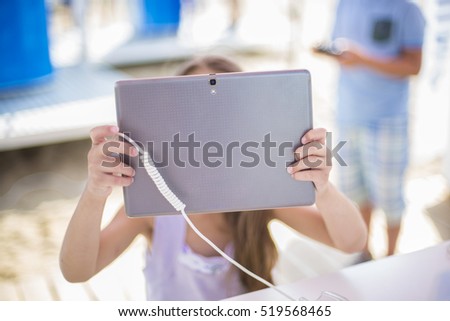 Little girl playing on tablet outdoor. Kid taking picture outside. Teenager with technology generation. Using tablet device.