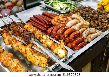 Assorted German sausages grilled in a steel container. Street food market Royalty-Free Stock Photo #519570598