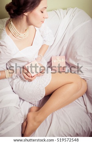 Joyful happy woman holding gift box over light chair bed background. Closeup image
