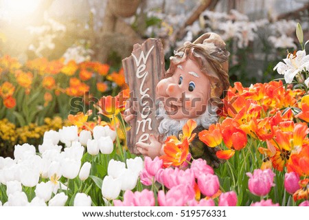 Doll dwarf holding a welcome sign among flowers