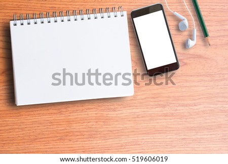 Blank notebook, smart phone and earphone on wooden table top view with copy space