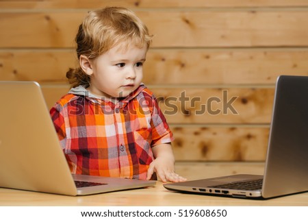 Cute baby boy child with blond curly hair plays on two laptop computers on wooden background