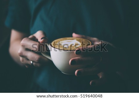 Hands of young woman holding a cup of coffee in a cafe. Toned picture