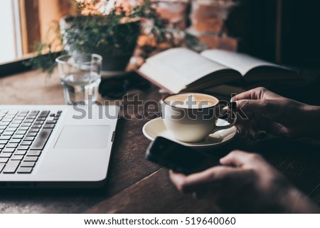 Young woman having a cup of coffee and holding a smart phone  in a cafe. Toned picture