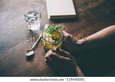 Hands of young woman holding a cup of hot mint tea or hot lemonade. Toned picture