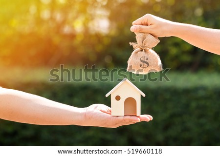 Loans for real estate concept, a man and a women hand holding a money bag and  a model home put together in the public park. Royalty-Free Stock Photo #519660118