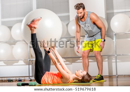 Young woman making exercise with fitball with personal trainer in the fitness room