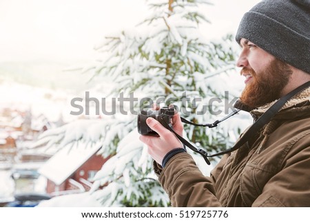 Profile of focused young man using camera and taking photos in winter