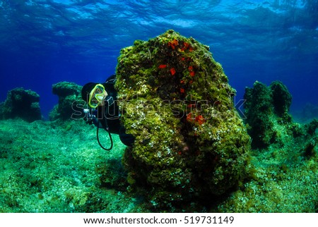 Scuba diver on the bottom of sea with water surface. Underwater photo of a man in scuba gear hiding behind a rock with water surface in the background. Shot in Adriatic sea - Croatia.