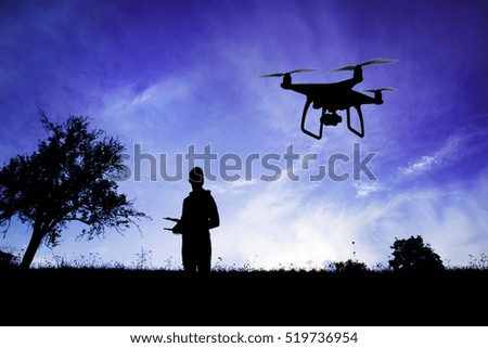Silhouette of man with flying drone in nature at dusk.
