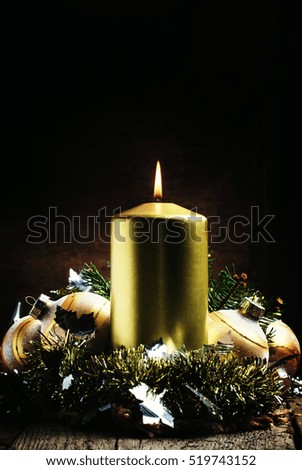 Golden burning candle, tinsel, Christmas balls, beads and spruce branches. New Year composition. Vintage dark wood background, selective focus