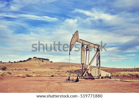 Retro toned picture of an oil pump, old industrial equipment on arid soil.