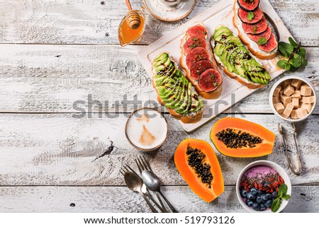 Healthy breakfast ingredients. Bowl of smoothie, fresh papaya, avocado and figs sandwiches , coffee and honey. Top view, copy space