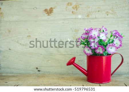 The red watering can with purple flowers on the wood table.