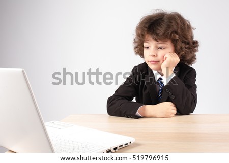 Little curly-haired businessman sitting at the table and looking thoughtfully into the laptop. Gray background.