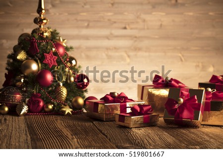 Golden presents with red ribbon under christmas tree. Wooden background and table.
Red and gold. Place for typography and logo. Copy space. 