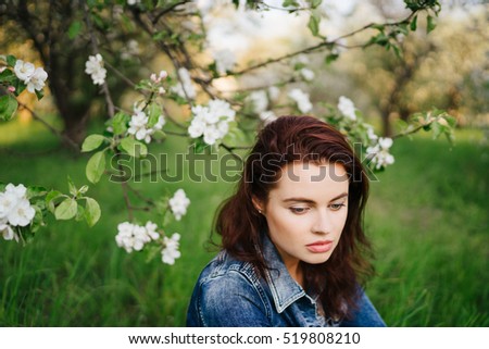 Young pretty serious caucasian woman in jeans jacket standing near blooming spring tree. Youth, freshness, beauty, happiness concept.