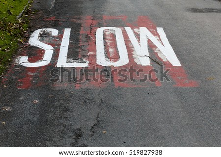Old road SLOW road markings sign with worn and faded red background with new painted letters