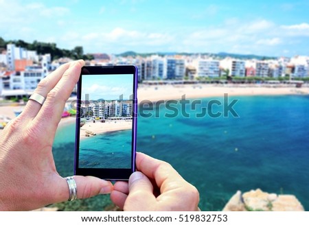 View over the mobile phone display during taking a picture of Costa Brava beach in Blanes town. Holding the mobile phone in hands and taking a photo. Focused on mobile phones screen. 