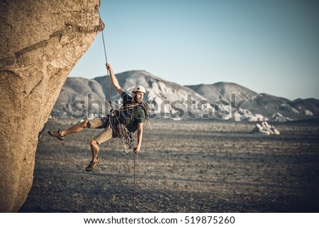 A rock climber rappelling past an overhang in Joshua Tree National Park, California, on a summer evening. Royalty-Free Stock Photo #519875260