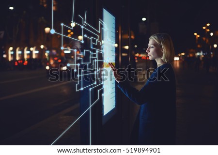 Young woman touching sensitive screen while selecting surface option. Female standing at big display with advanced innovative device with infographics design elements.Person with futuristic technology Royalty-Free Stock Photo #519894901