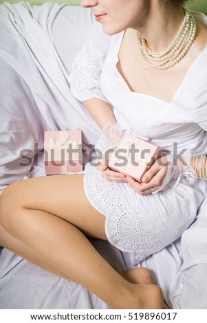 Joyful happy woman holding gift box over light chair bed background. Closeup image