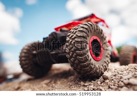 Red crawler wheels outside close-up. Rc car standing on rock, blue sky with clouds on background Royalty-Free Stock Photo #519953128