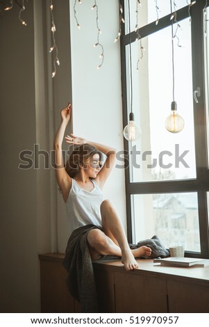 girl sitting on a window in a blanket with a mug of coffee and a magazine