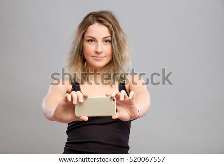 Expressive young woman taking pictures through cellphone, over gray background