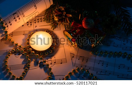 Christmas decorations, burning candle and sheet music in the dark