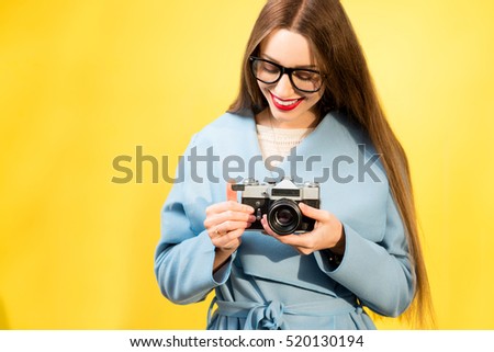 Stylish woman photographer with retro camera on the yellow wall background