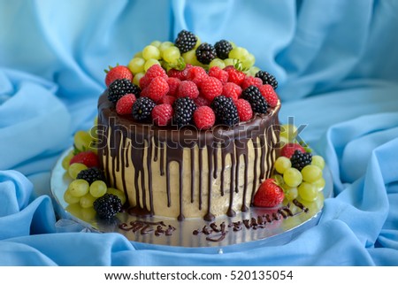 Chocolate cake with caramel cream, decorated chocolate glaze, berries and fruits on the blue background