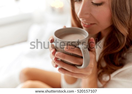 morning, coziness, winter and people concept - close up of happy young woman with cup of coffee or cocoa drink in bed at home