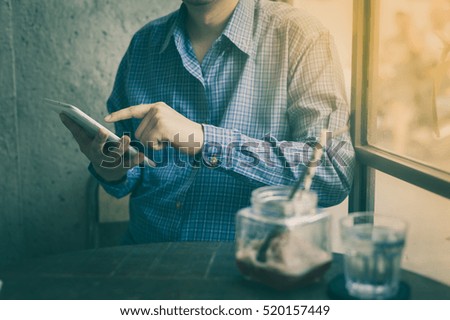 Adult man using small tablet pc beside a glass of water in cafe on weekend afternoon. Businessman lifestyle on weekend with technology concept with vintage filter effect