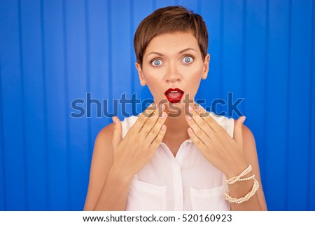 Wow! Shock! Amazed young woman standing against blue wall.