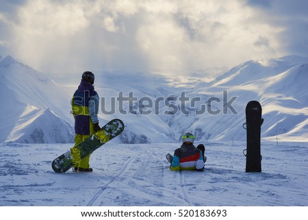 Snowboarders have a rest and look at the winter mountains landscape.