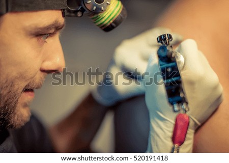 Artist making tattoo on male customer's shoulder in studio