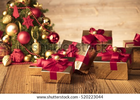 Golden presents with red ribbon under christmas tree. Wooden background and table. Red and gold. Place for typography and logo. Copy space.