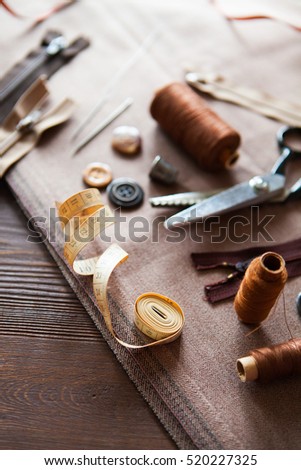 Scissor, buttons, zip, tape measure, thread and thimble on fabrics on dark wooden background, flat lay. Set