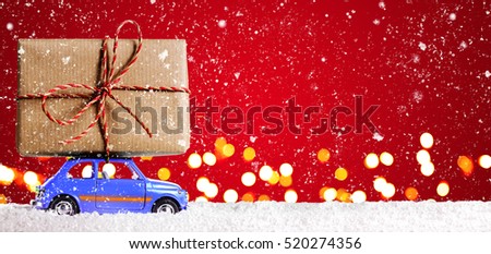 Blue retro toy car delivering Christmas or New Year gifts on festive red background