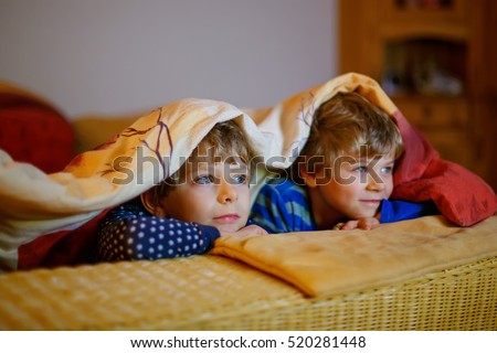 Happy little brothers, adorable kid boys watching television while lying. Funny children enjoying cartoons