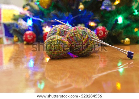 Balls of yarn and knitting needles. Christmas tree in the background.